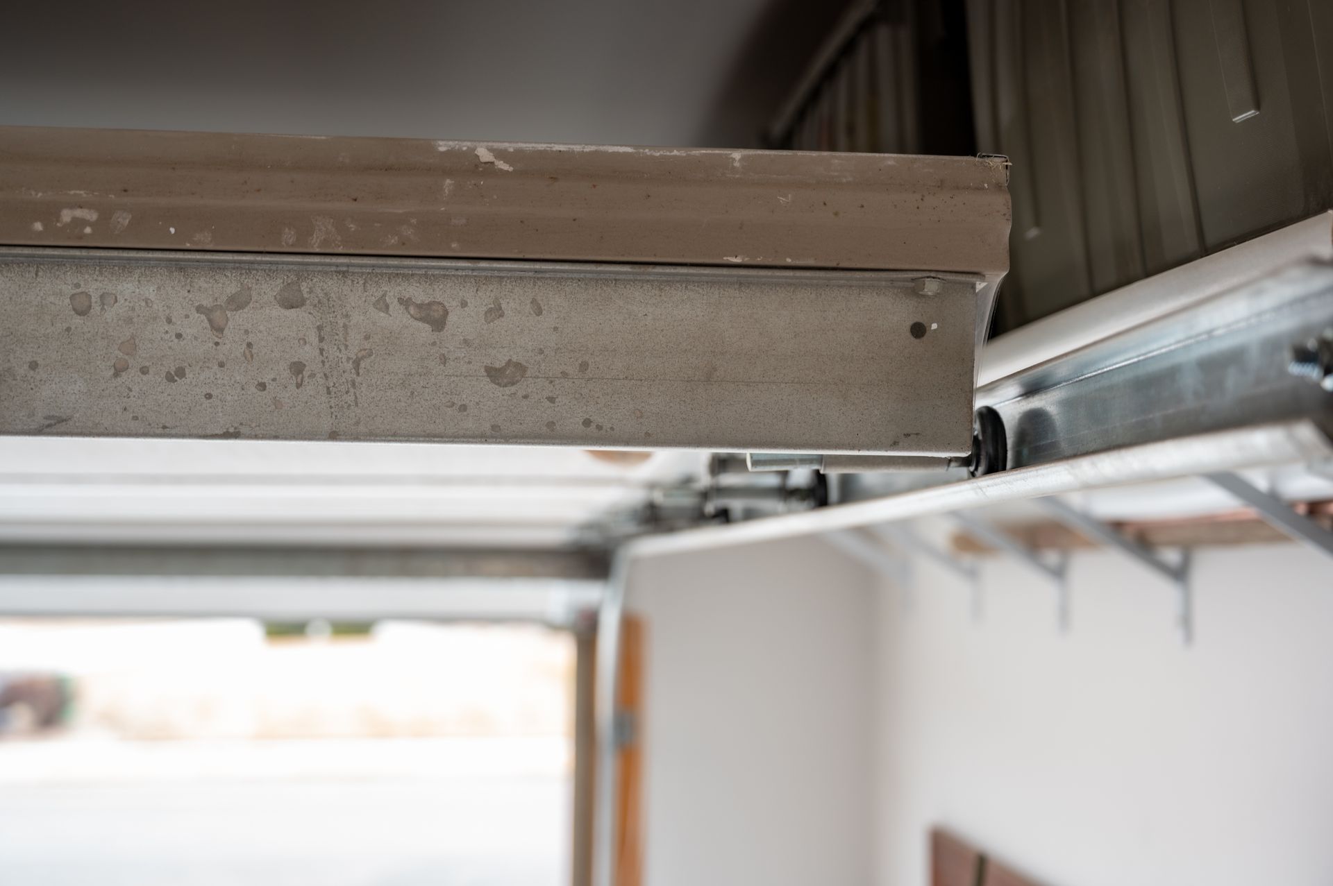 Close-up of a garage door track and overhead opener mechanism with metal rails and ceiling beams. Close-up of a garage door track and overhead opener mechanism with metal rails and ceiling beams.