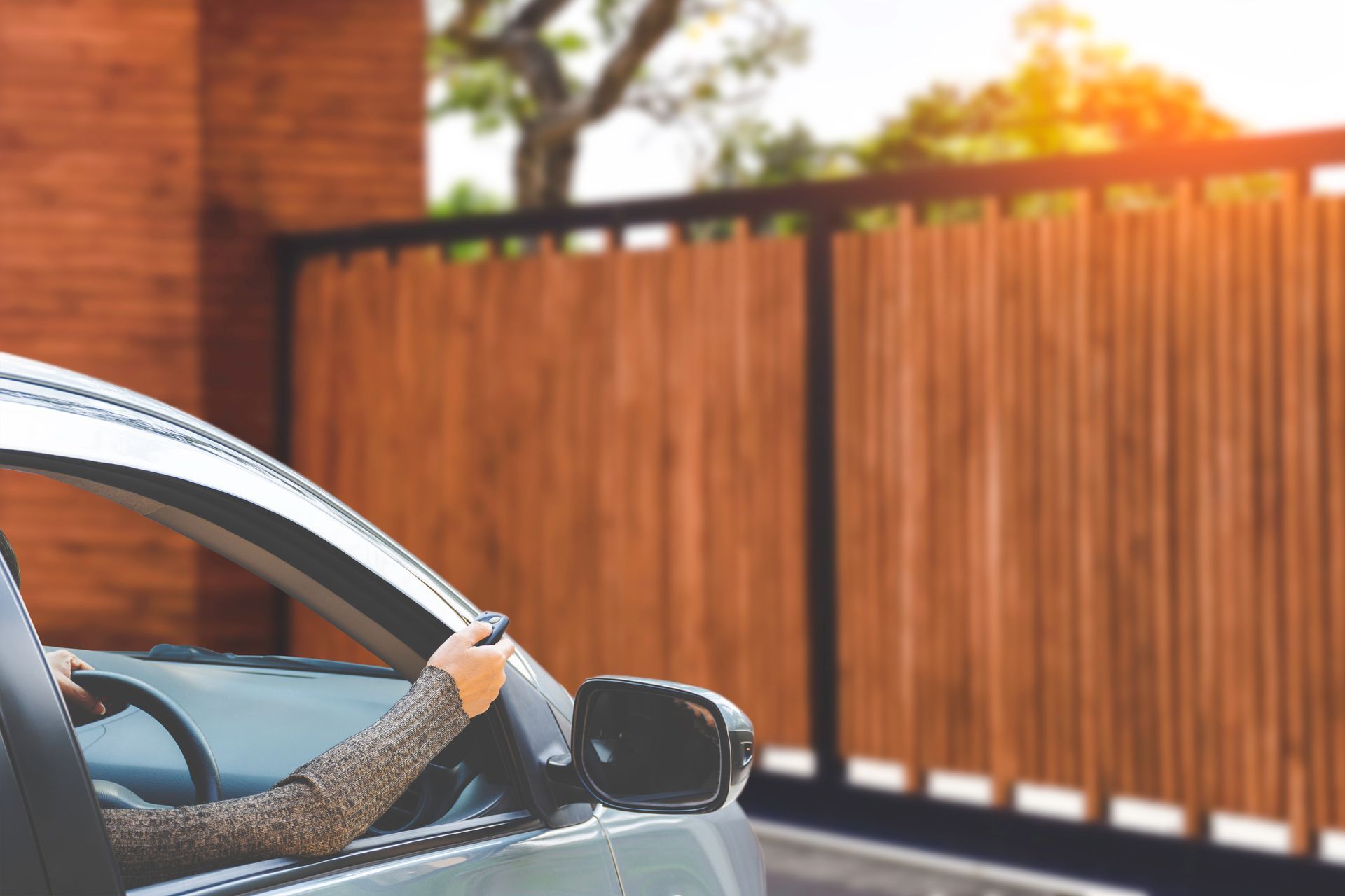 Person driving a silver car past a wooden fence in warm sunlight