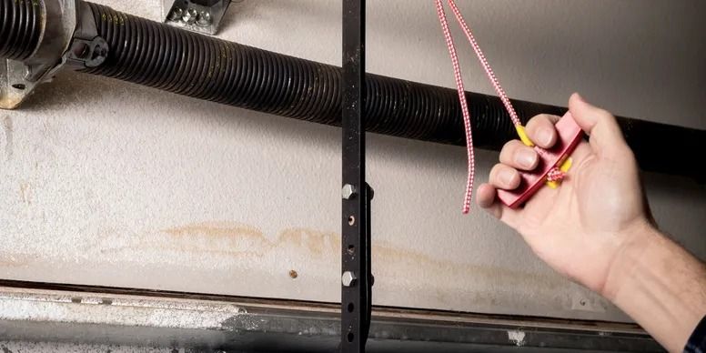 Hand holding a yellow flashlight and red cord near a garage door spring mechanism Hand holding a yellow flashlight and red cord near a garage door spring mechanism