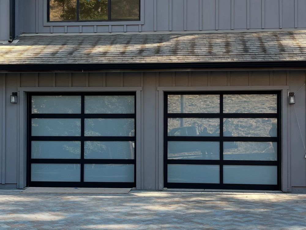 Two black-framed garage doors on a gray house exterior, viewed from the driveway