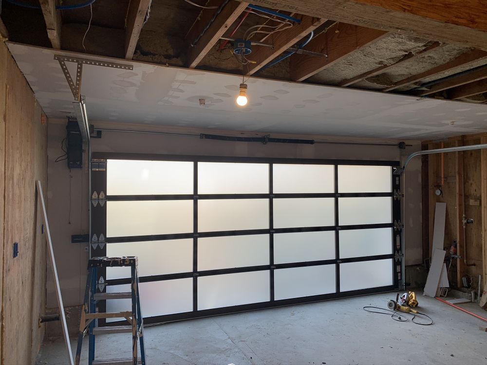 Partially finished garage with frosted glass garage door, exposed studs, and a ladder on the left Partially finished garage with frosted glass garage door, exposed studs, and a ladder on the left