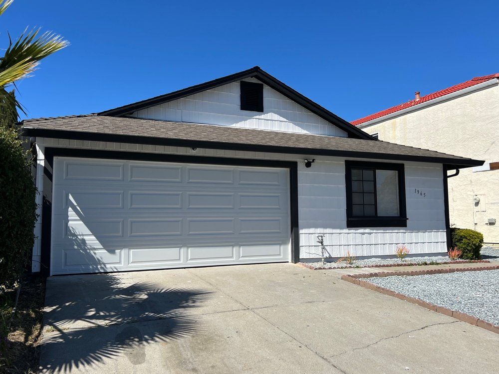 Single-story house with a two-car garage, white trim, and a driveway in bright sunlight