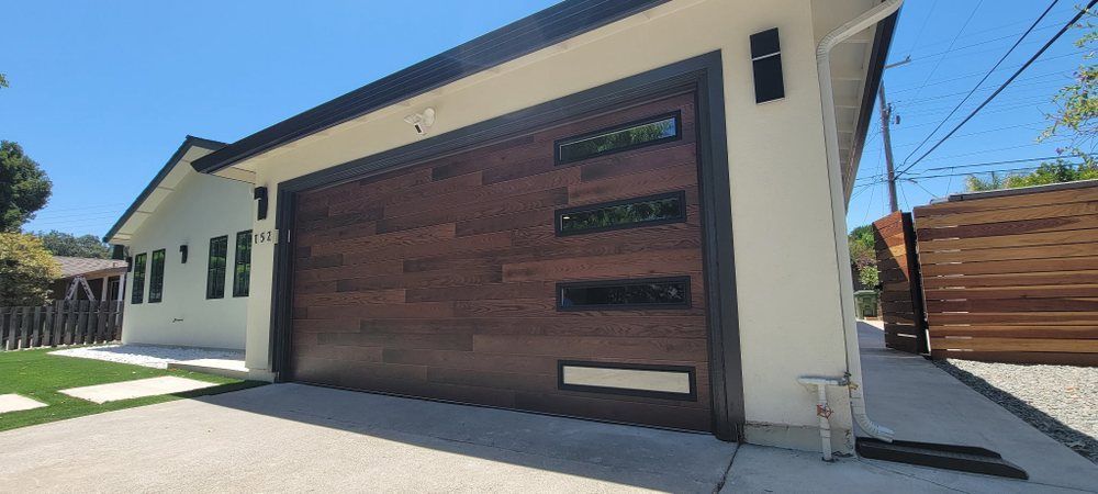 Modern home exterior with a large wood garage door and white stucco walls in bright sunlight