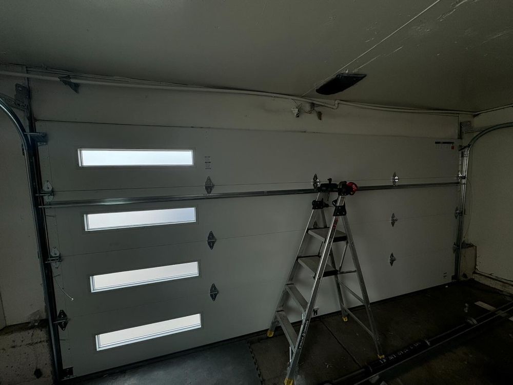 Garage interior with a ladder-mounted camera setup aimed at a closed sectional door.