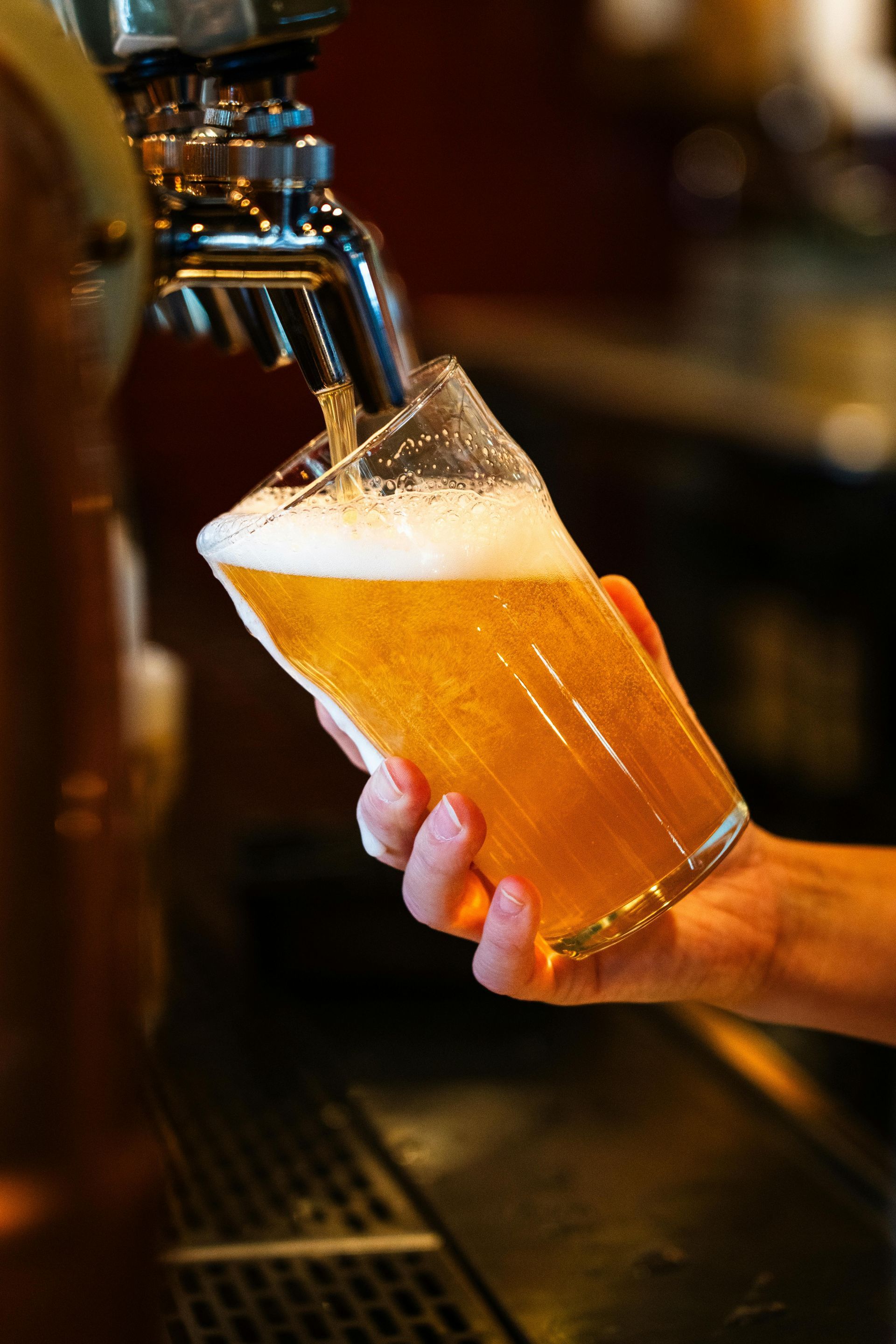 Hand holding a glass while beer is poured from a tap, creating a foamy head.