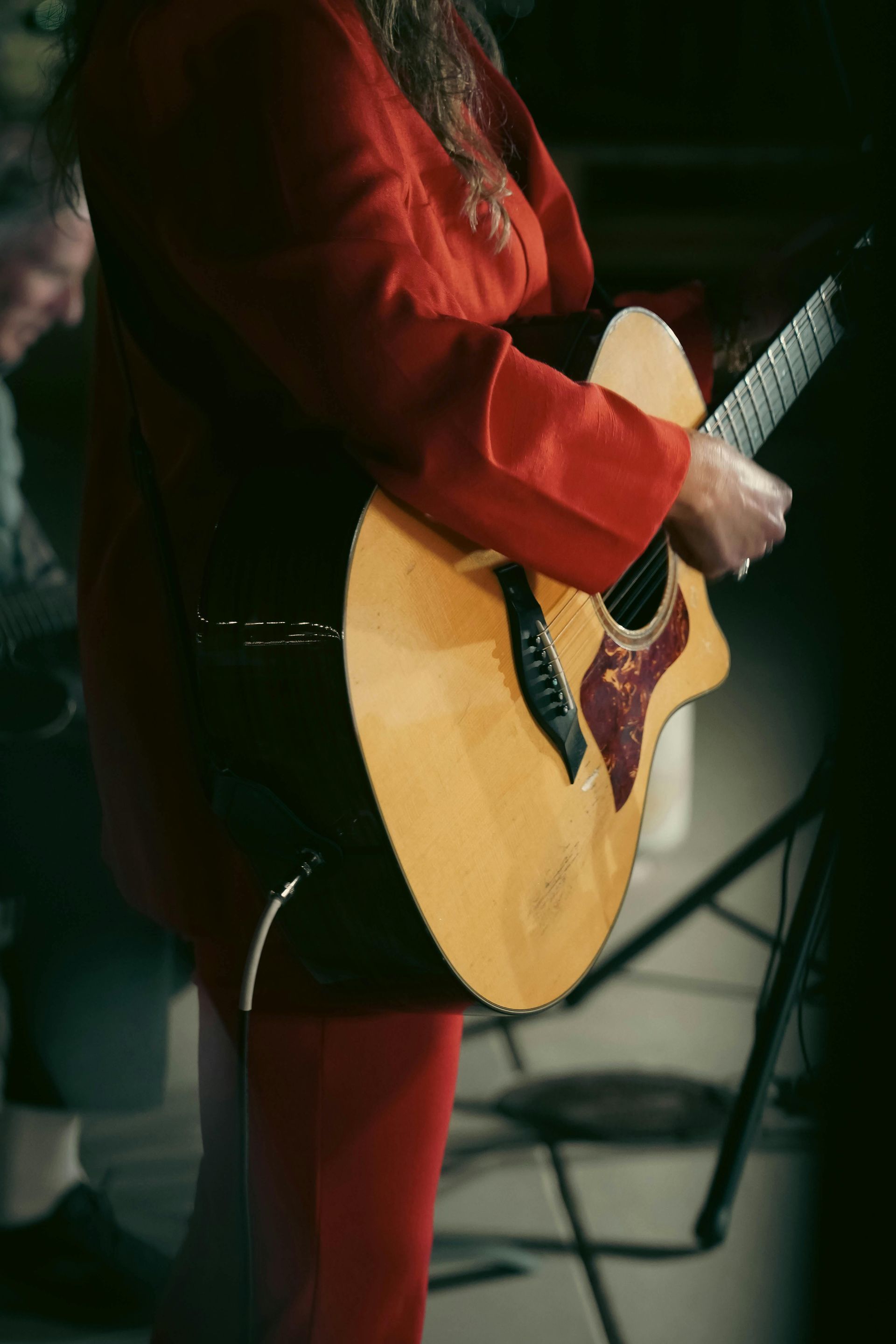 Person in red outfit playing acoustic guitar onstage.