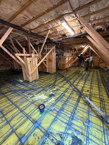 Underside of a wooden building with steel support columns on concrete footings and yellow jacks on a dirt floor