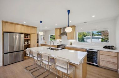 Modern kitchen with island, gas range, and large windows opening to a bright backyard patio