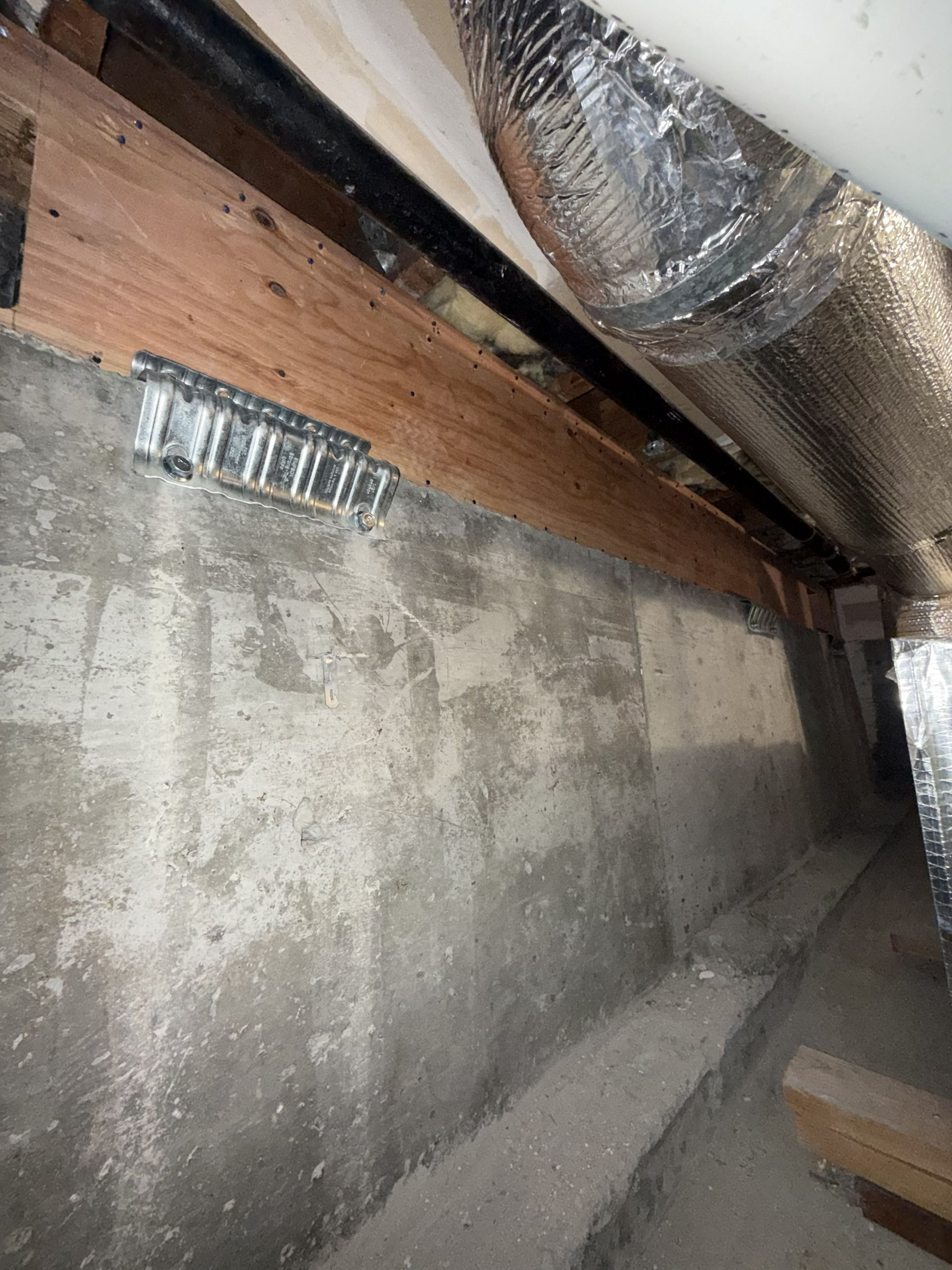 Plywood wall over concrete foundation with metal conduit in an unfinished building interior