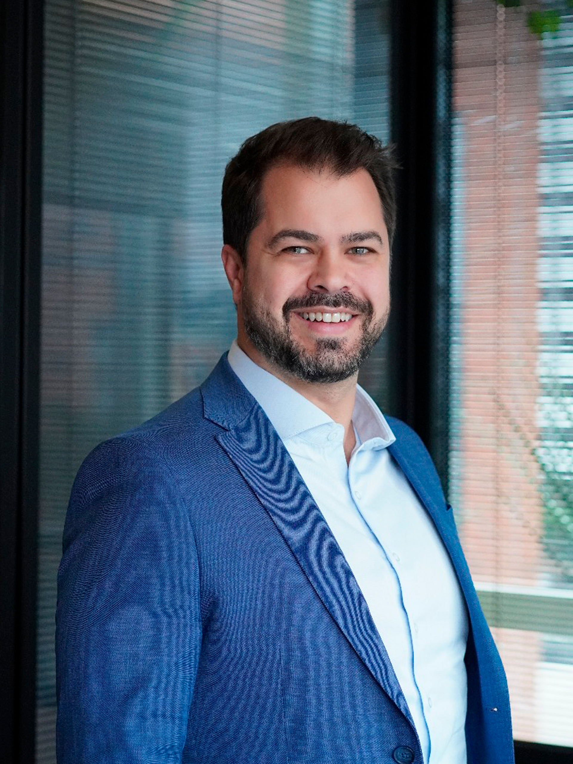 Um homem de terno azul e camisa branca está parado em frente a uma janela.