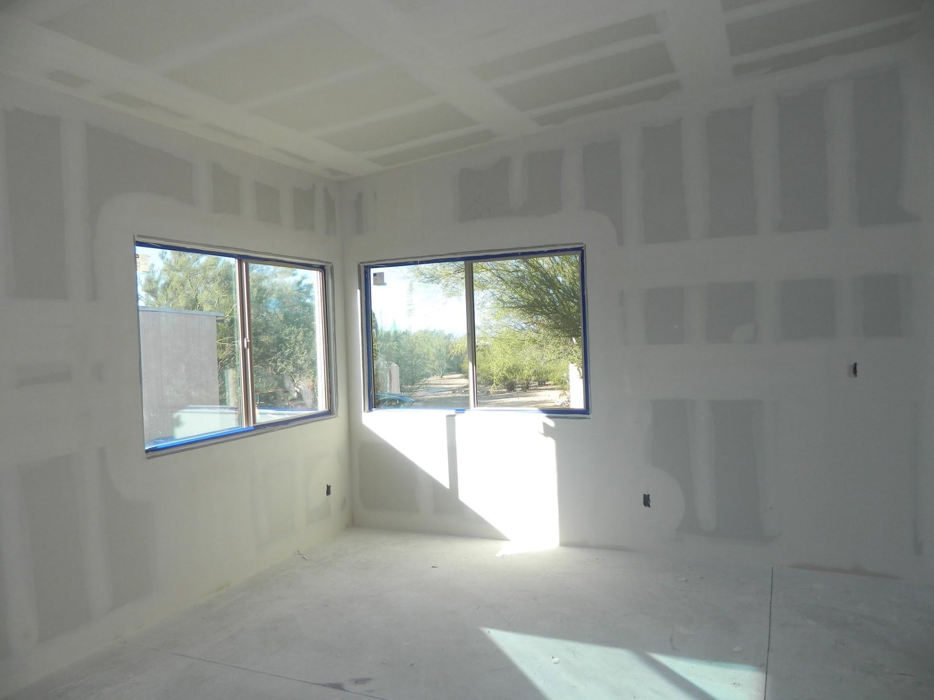 Empty unfinished room with white drywall, large windows, and sunlight on the floor