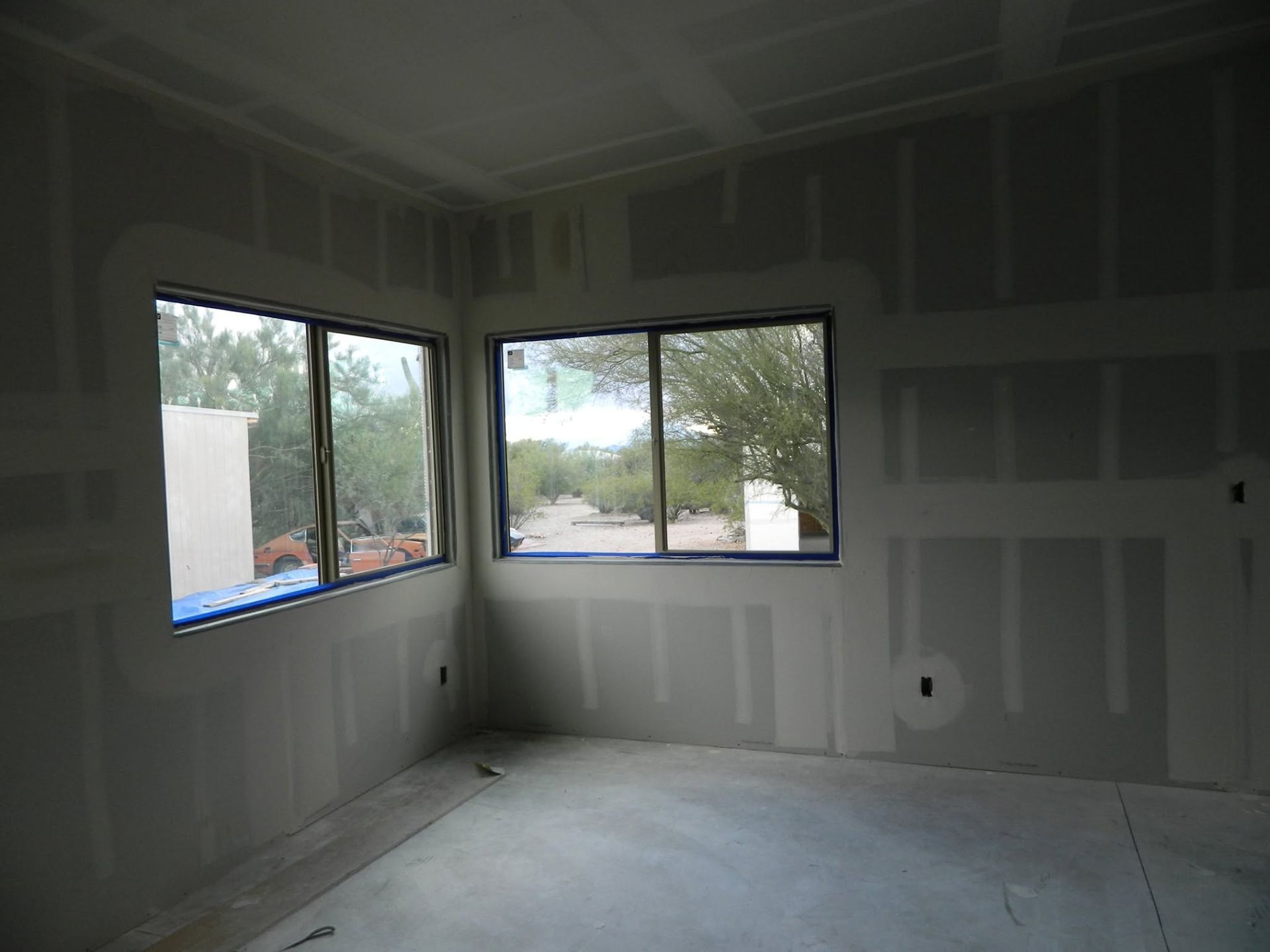 Unfinished room with drywall, three windows, and a concrete floor under construction.