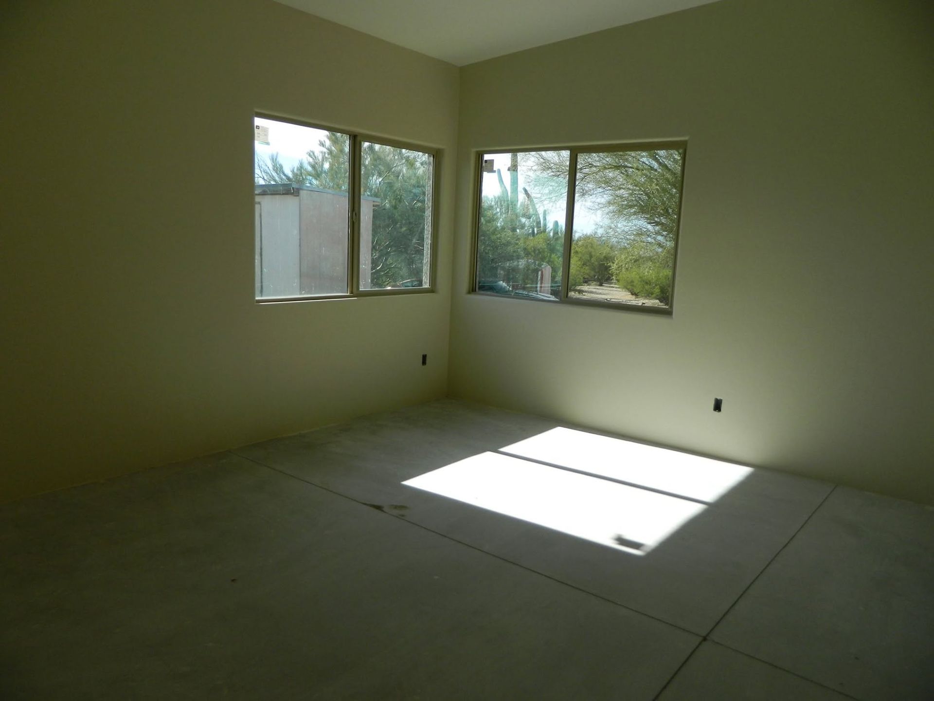 Empty unfurnished room with pale walls, tiled floor, and sunlight streaming through two windows.