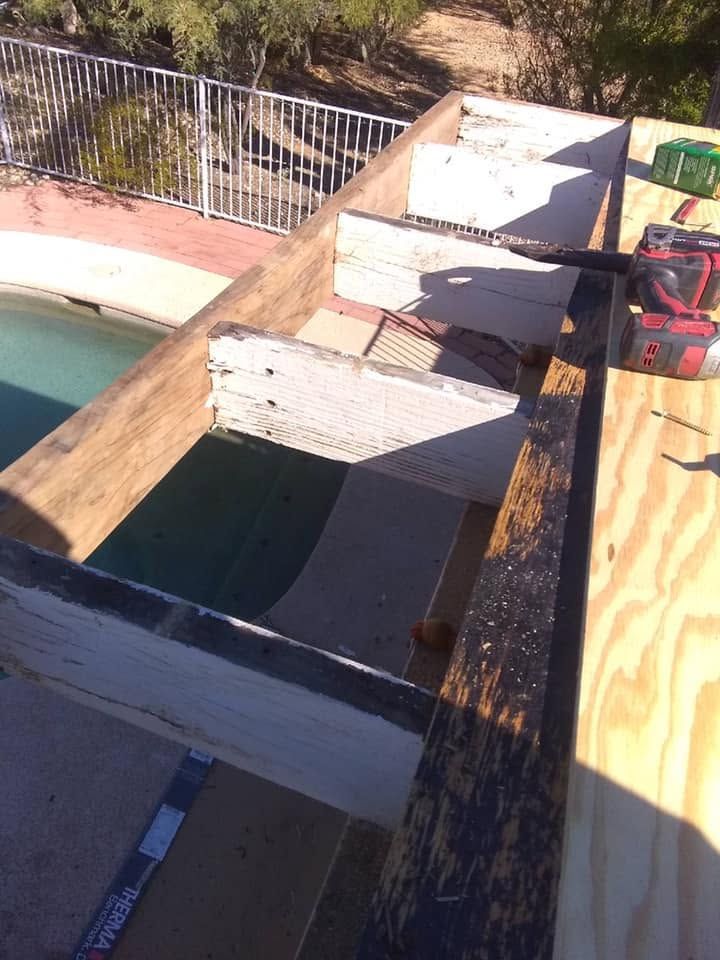 Broken wooden deck beside a swimming pool with scattered construction materials and tools