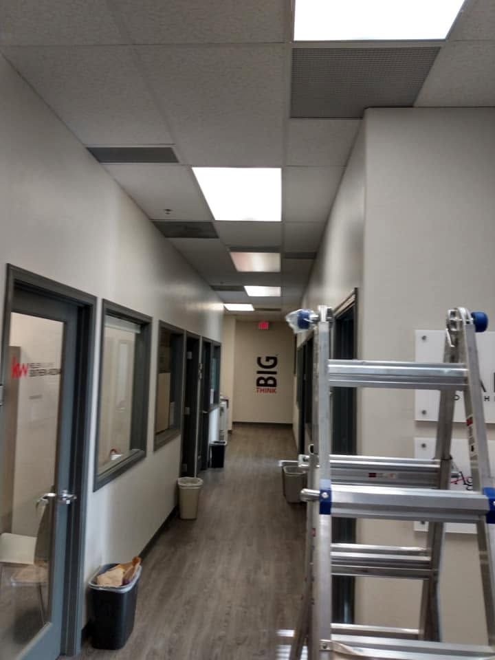 Narrow office hallway with windows, ceiling lights, ladder, and a trash can; BIG sign at the far end
