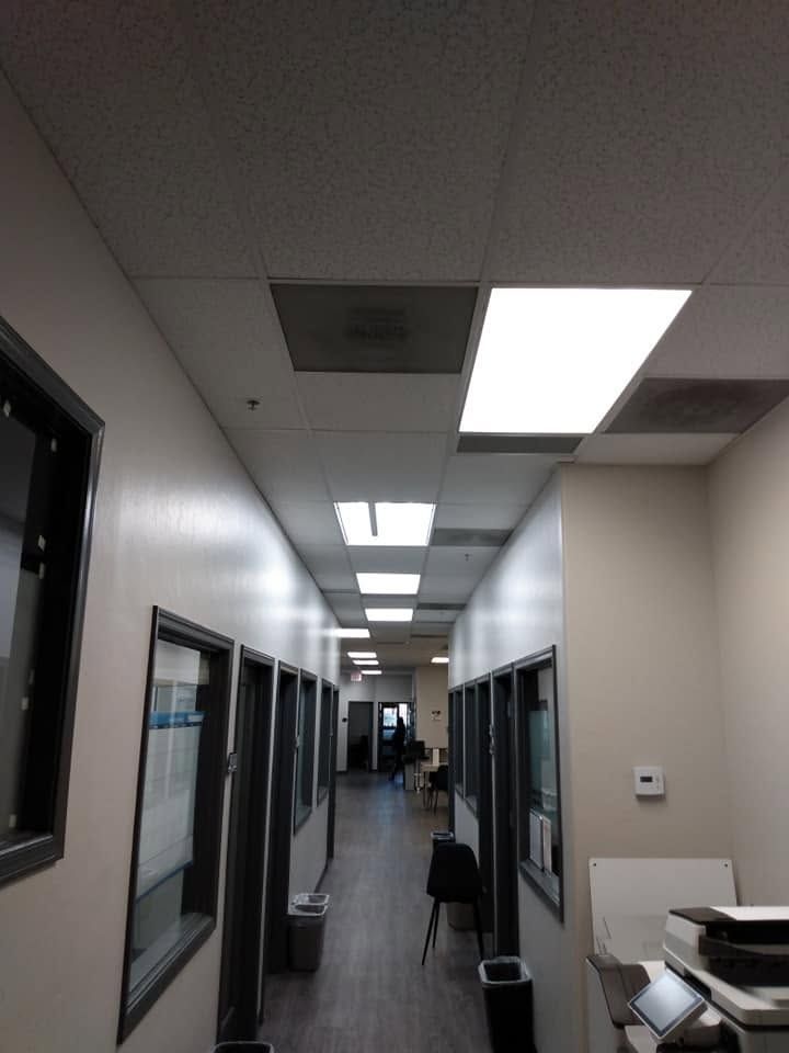 Empty office hallway with fluorescent ceiling lights, doors on both sides, and a chair near the end.