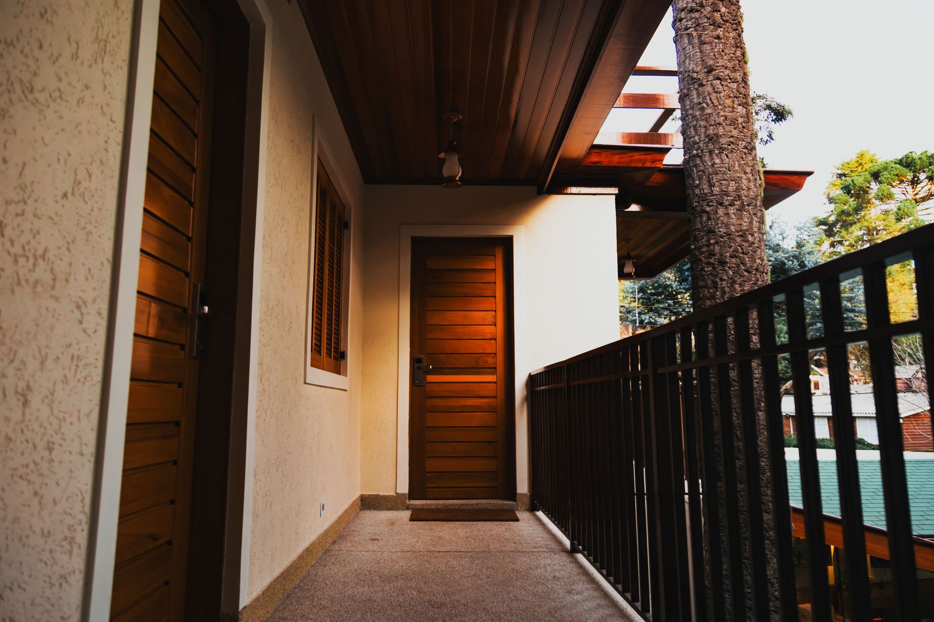 Covered apartment walkway with wooden door, white walls, and black railing beside a pool