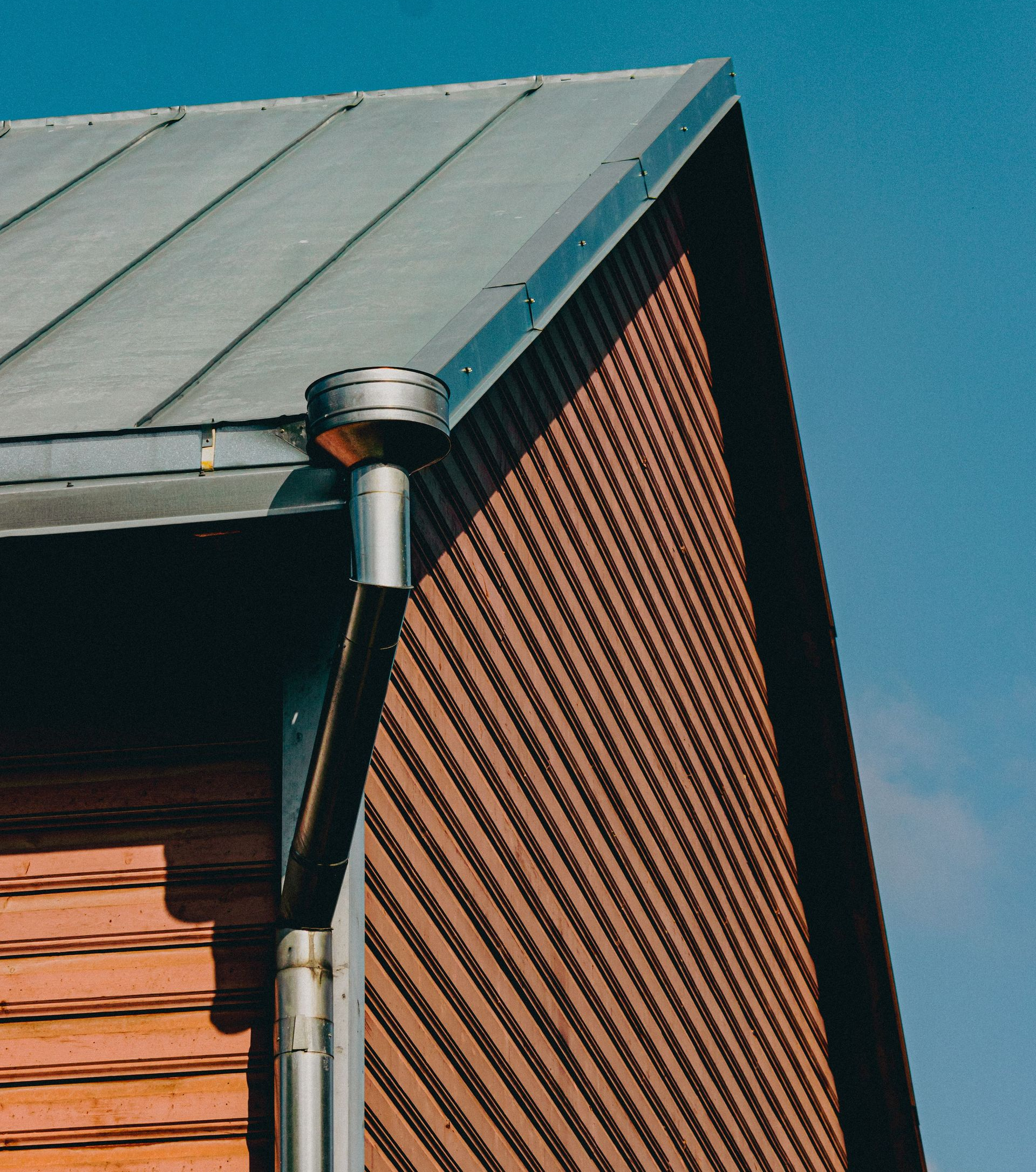 Roof gutter and downspout on a brick house against a blue sky