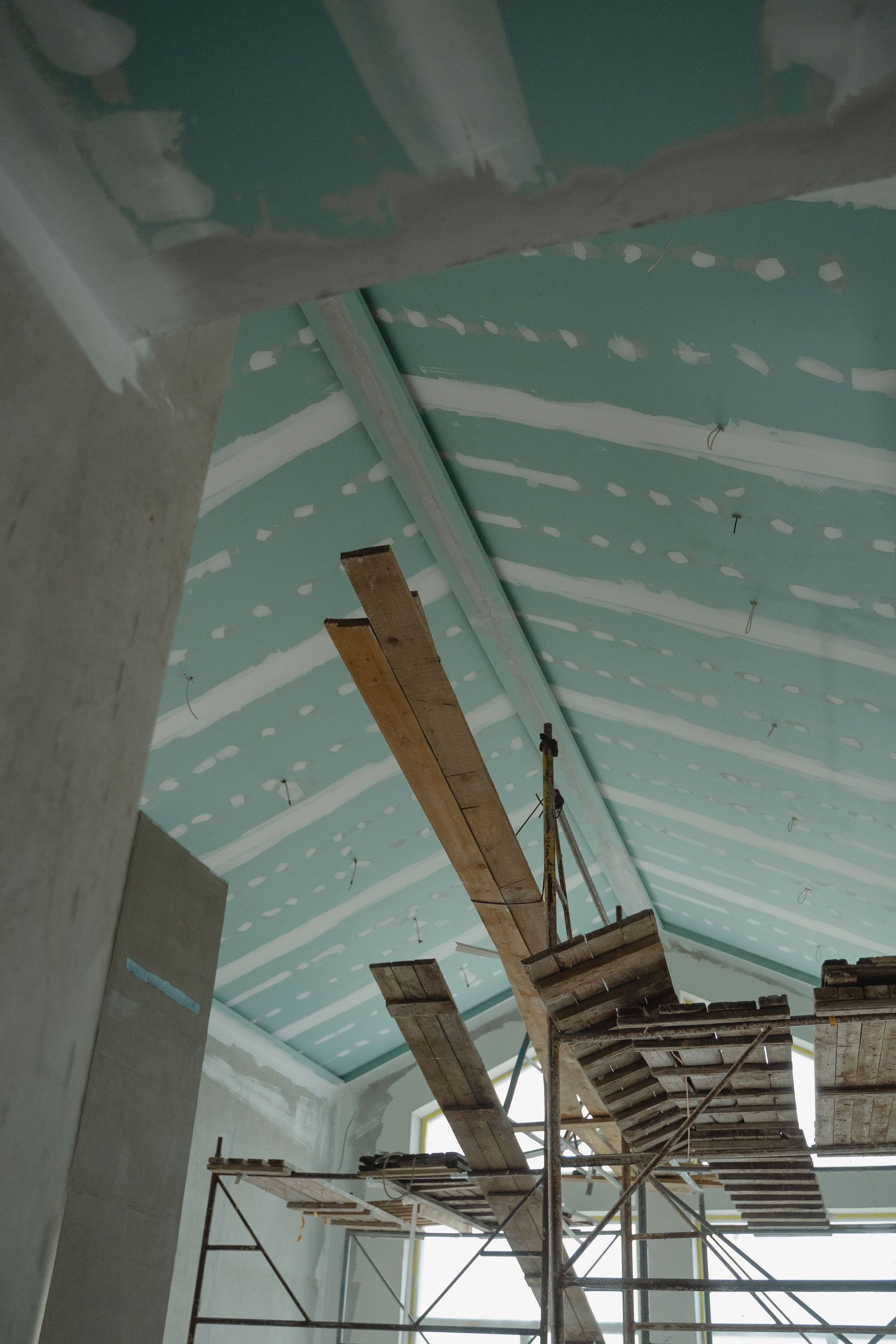 Interior ceiling under renovation with exposed beams, scaffolding, and hanging wooden planks.
