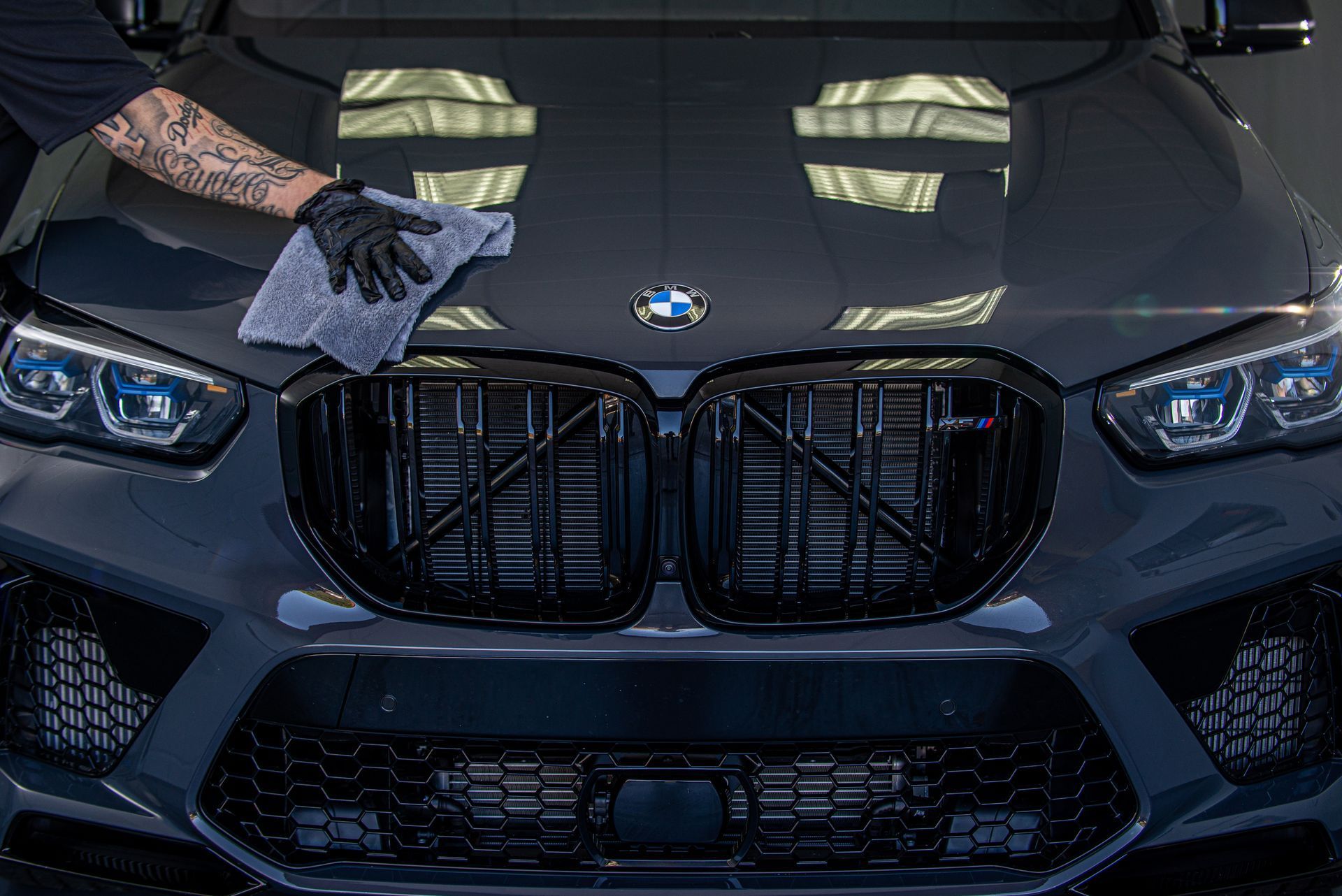 Person wiping down a dark gray BMW hood with a gray cloth and black gloves.