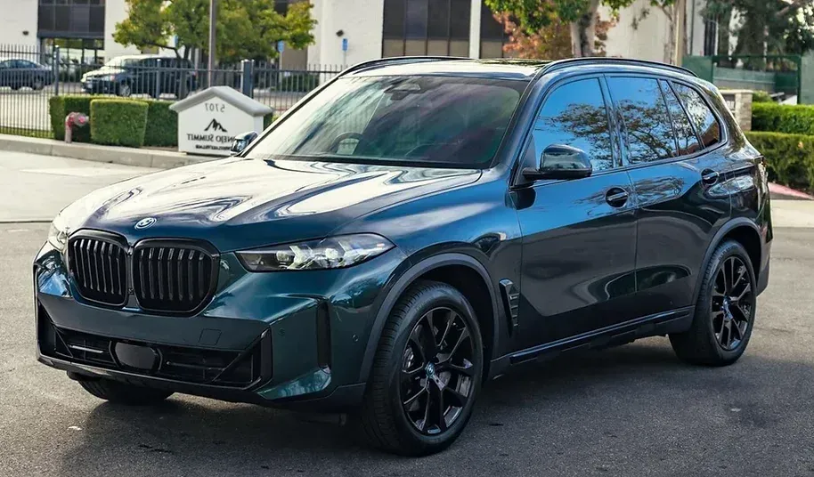 A bmw x5 is parked in a parking lot in front of a building.