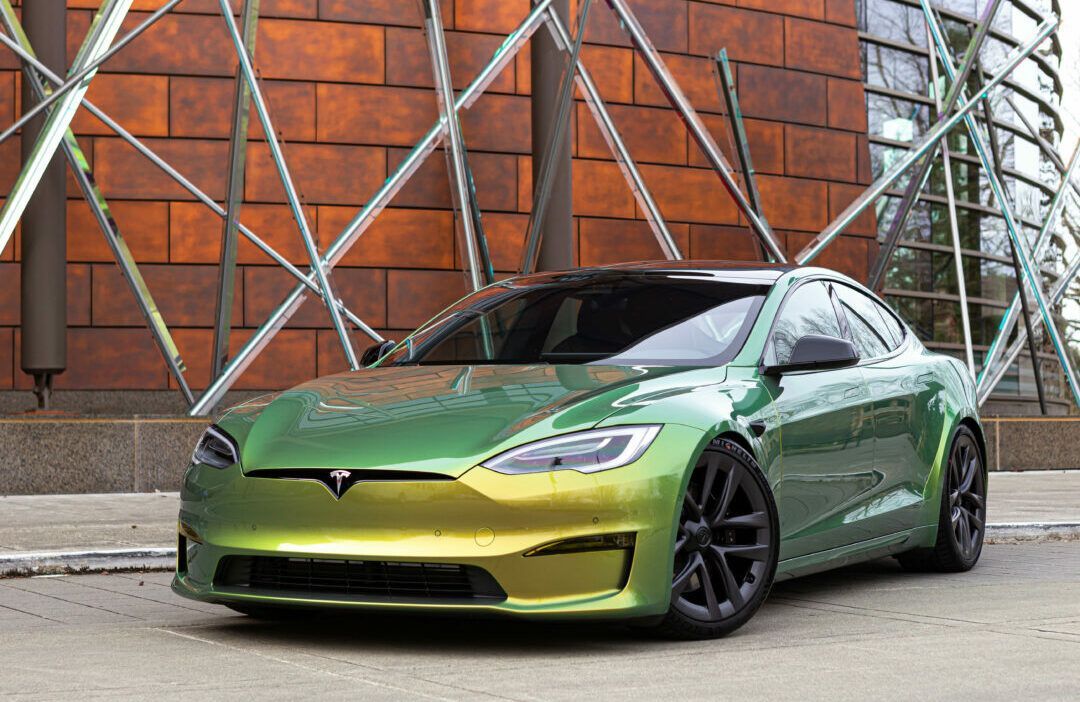 A green and yellow tesla model s is parked in front of a building.