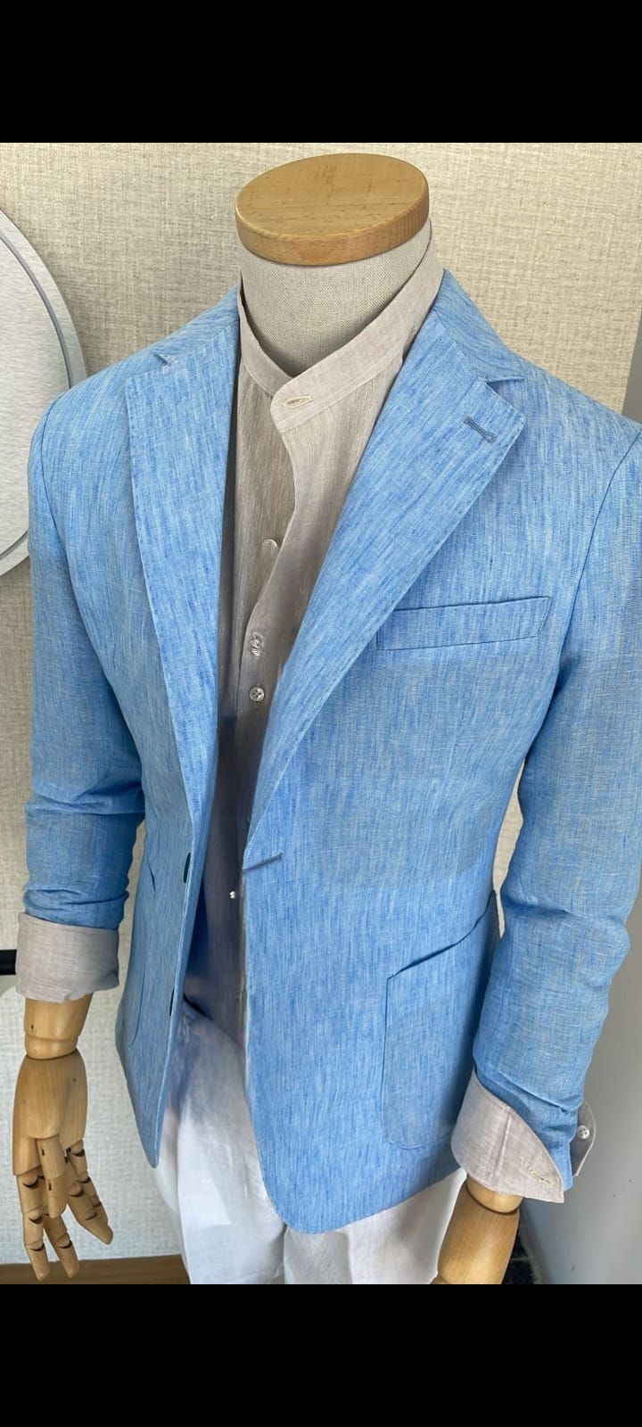 Manichino che indossa un blazer azzurro sopra una camicia bianca e pantaloni beige.