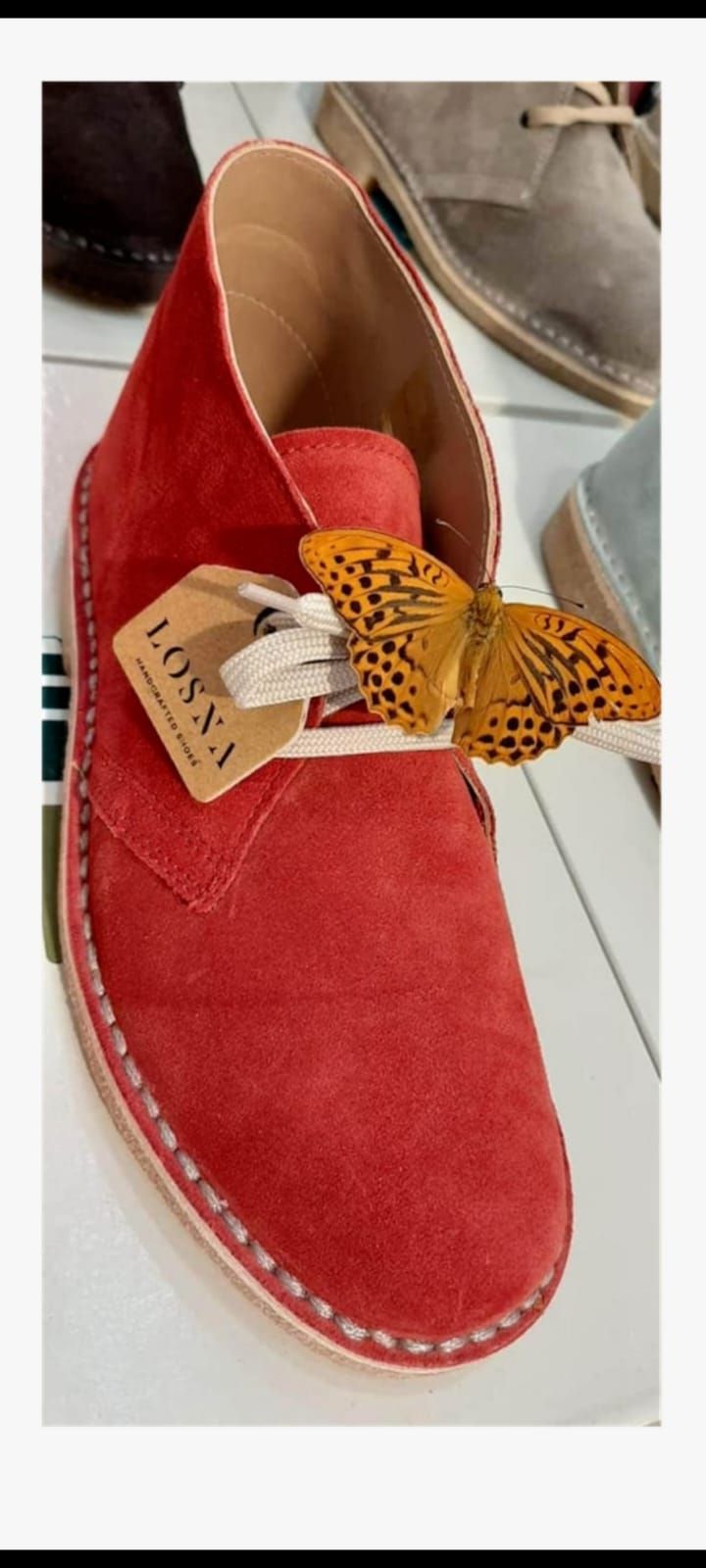 Scarpa slip-on in camoscio rosso con fiocco giallo a pois ed etichetta, fotografata in interni.