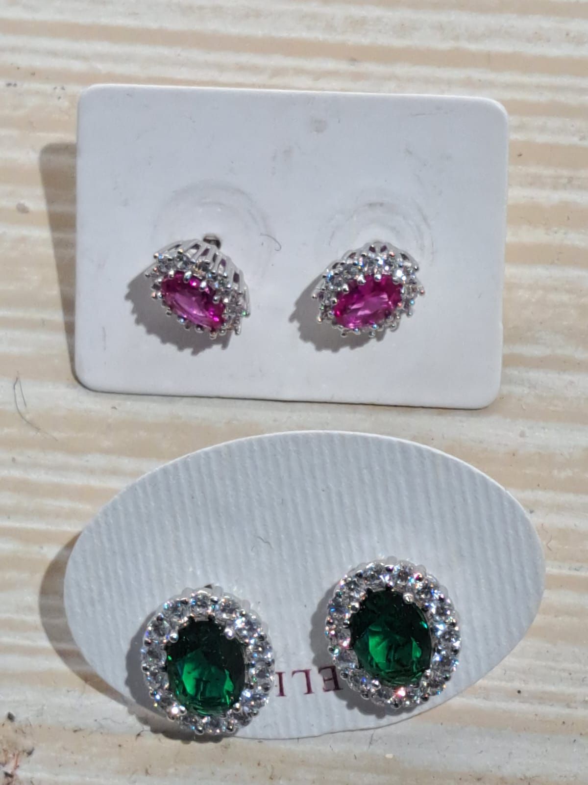 Due paia di orecchini a lobo ovali con pietre preziose: rosa su cartoncino bianco, verdi su cartoncino grigio.