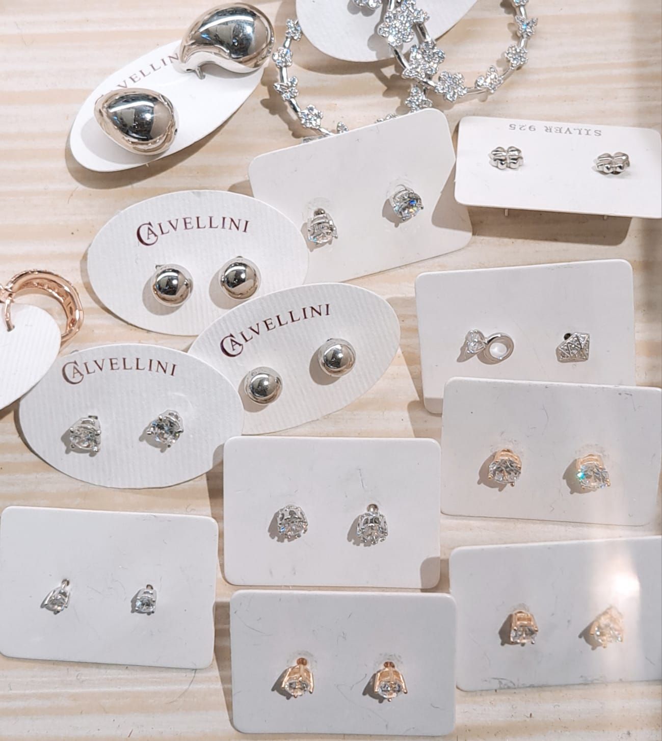 Assortimento di orecchini a perno in argento e oro esposti su cartoncini bianchi per gioielli su una superficie beige.