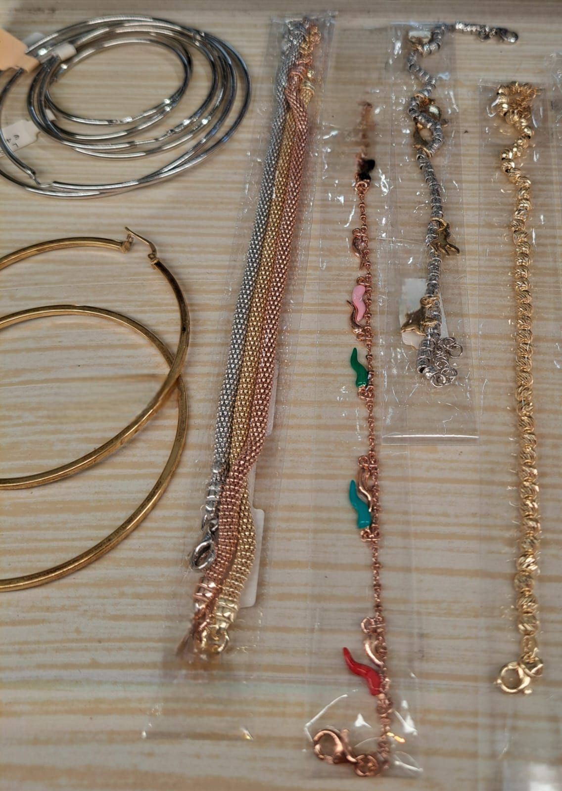 Su una superficie a righe sono disposte diverse collane e bracciali, tra cui catene in argento, oro e con perline.