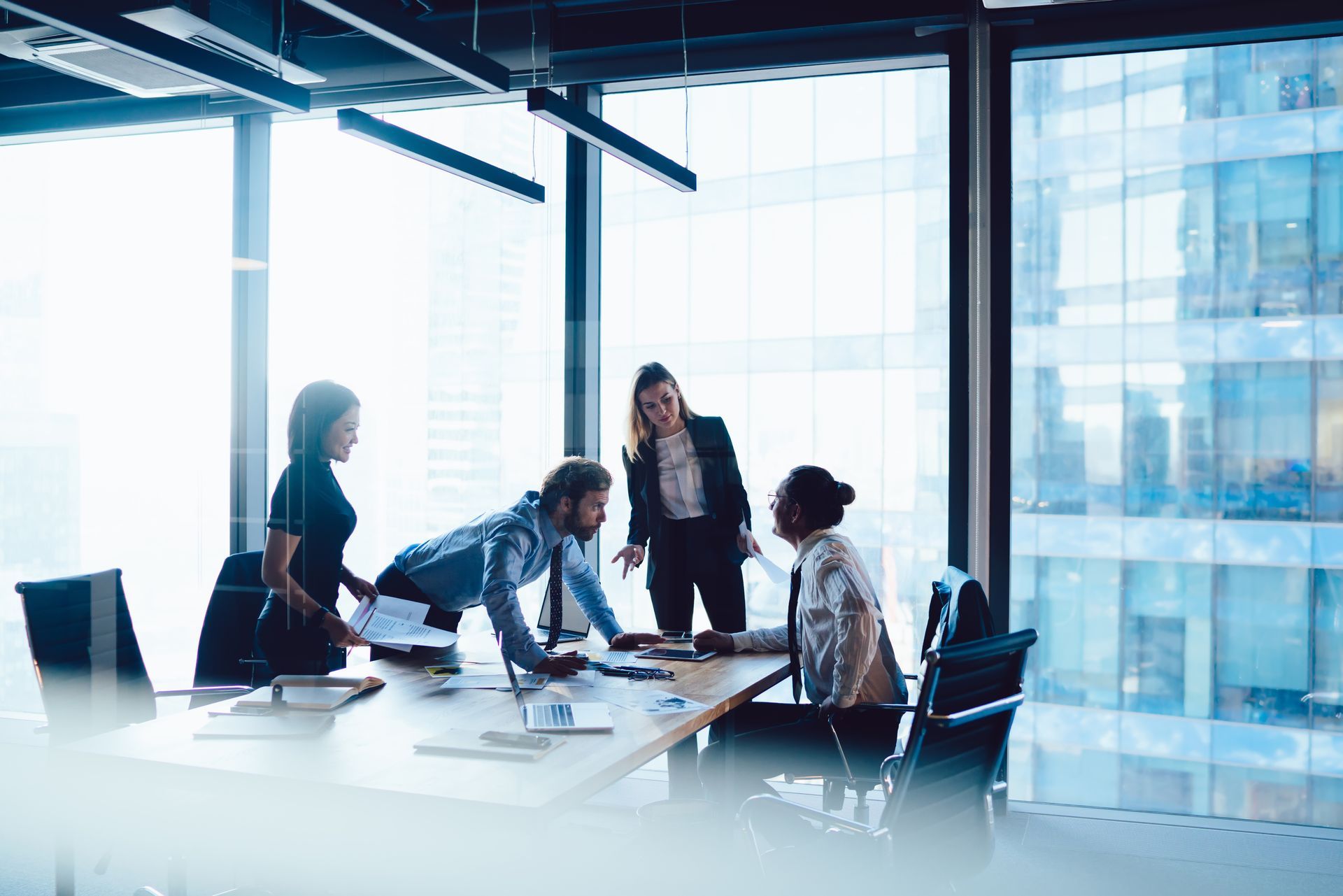 A diverse group of professionals in a brightly lit modern office boardroom, actively collaborating around a table.