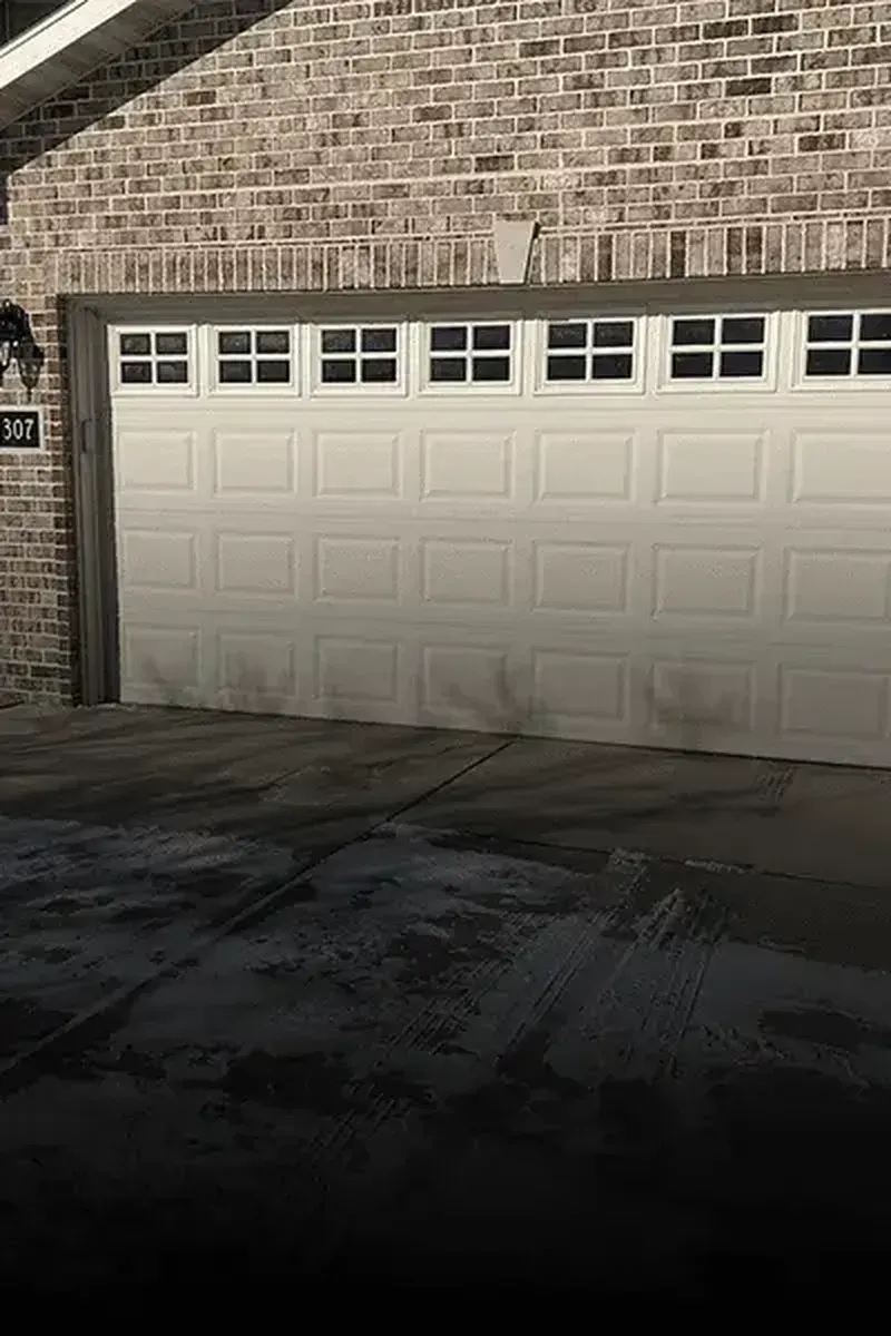 A white garage door with a row of small windows across the top, set into a brick house exterior.
