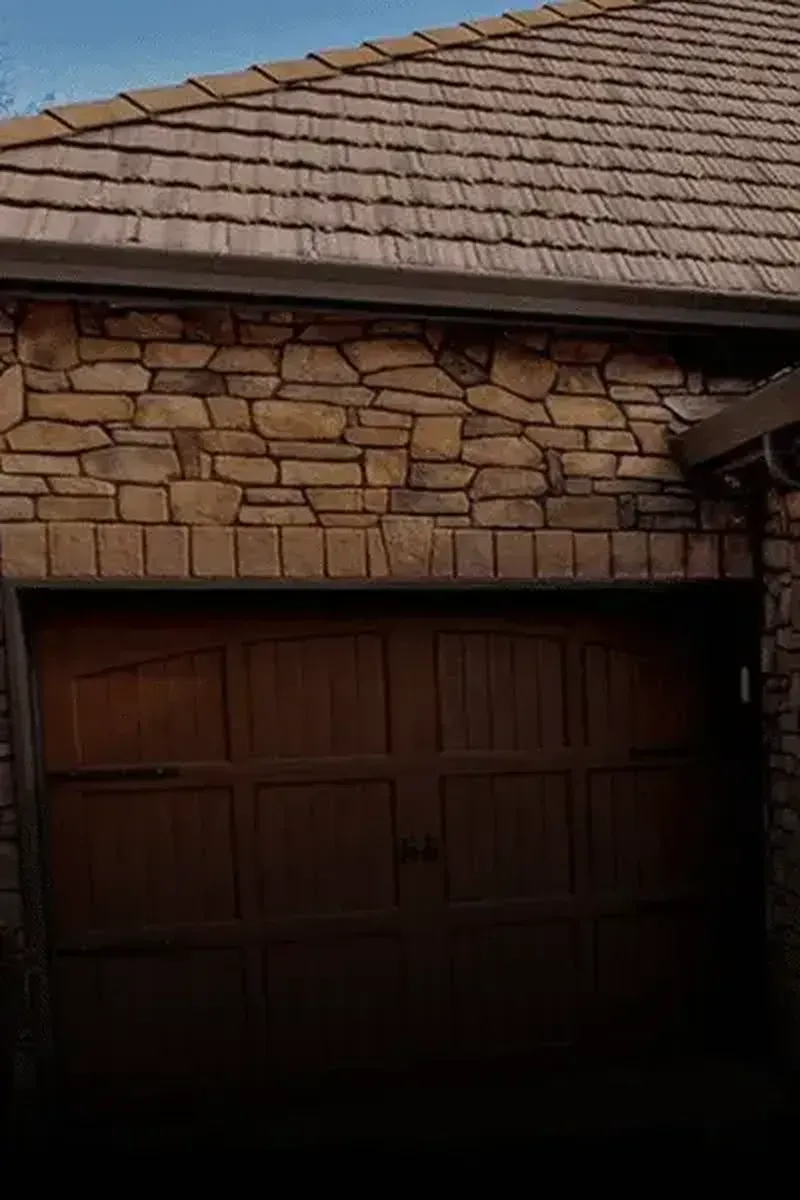A dark wooden garage door below a stone-walled exterior and a tiled roof.