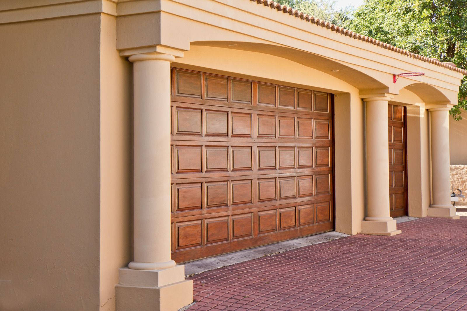 Beige house exterior with a closed wooden garage door and brick driveway