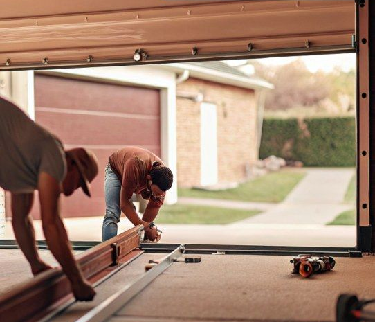 Workers installing a garage door track inside an open garage, with tools on the floor.