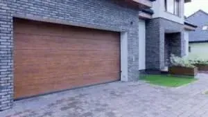 A modern house exterior featuring a wooden-paneled double garage door set into a grey brick facade.