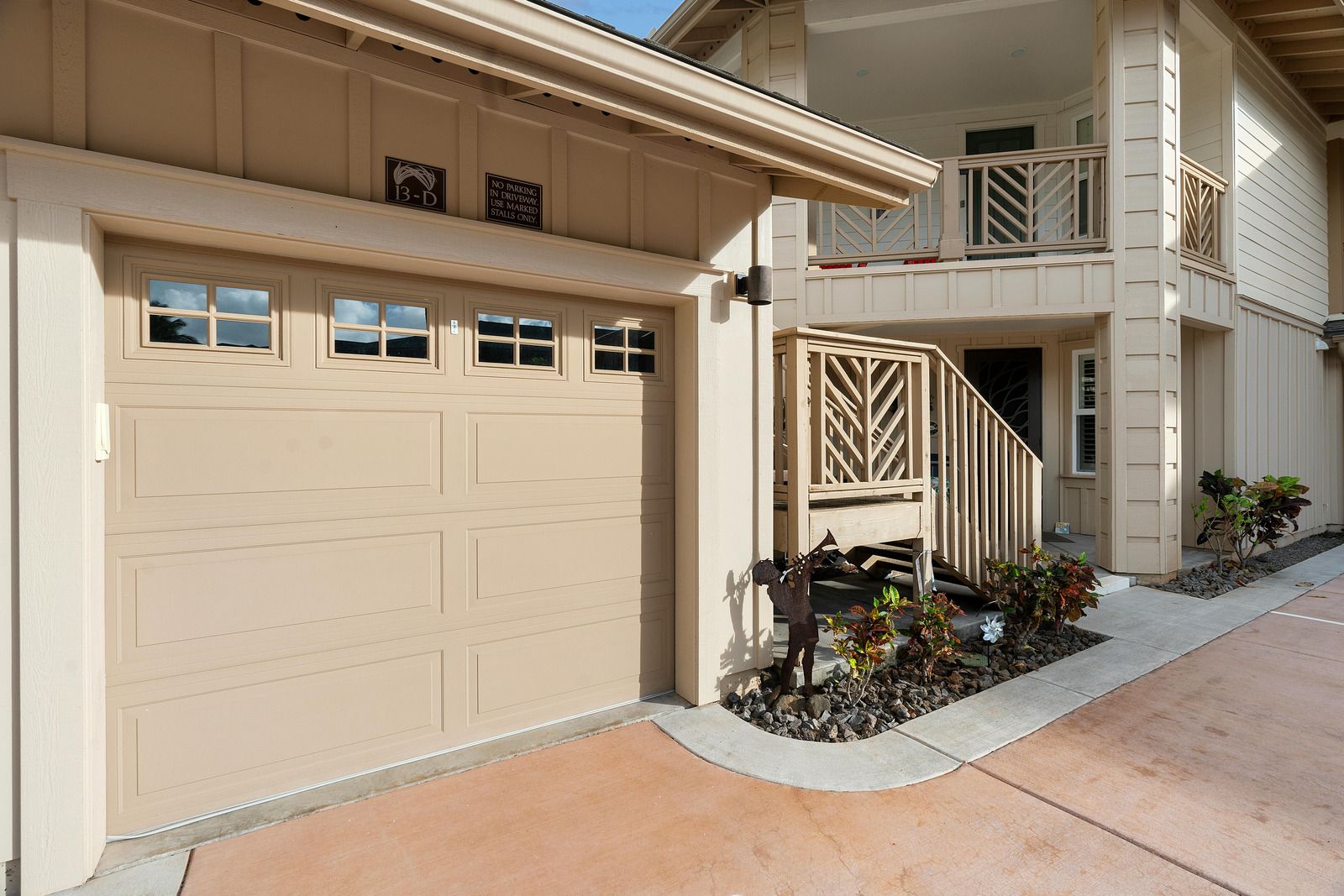Beige garage beside a townhouse walkway with a small landscaped entry and white stairway.