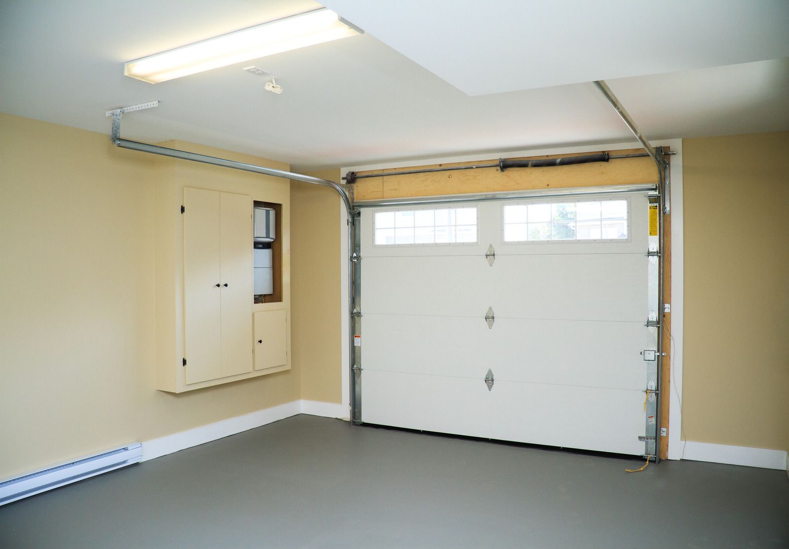 Empty garage with white overhead door, beige walls, utility box, and fluorescent ceiling light.