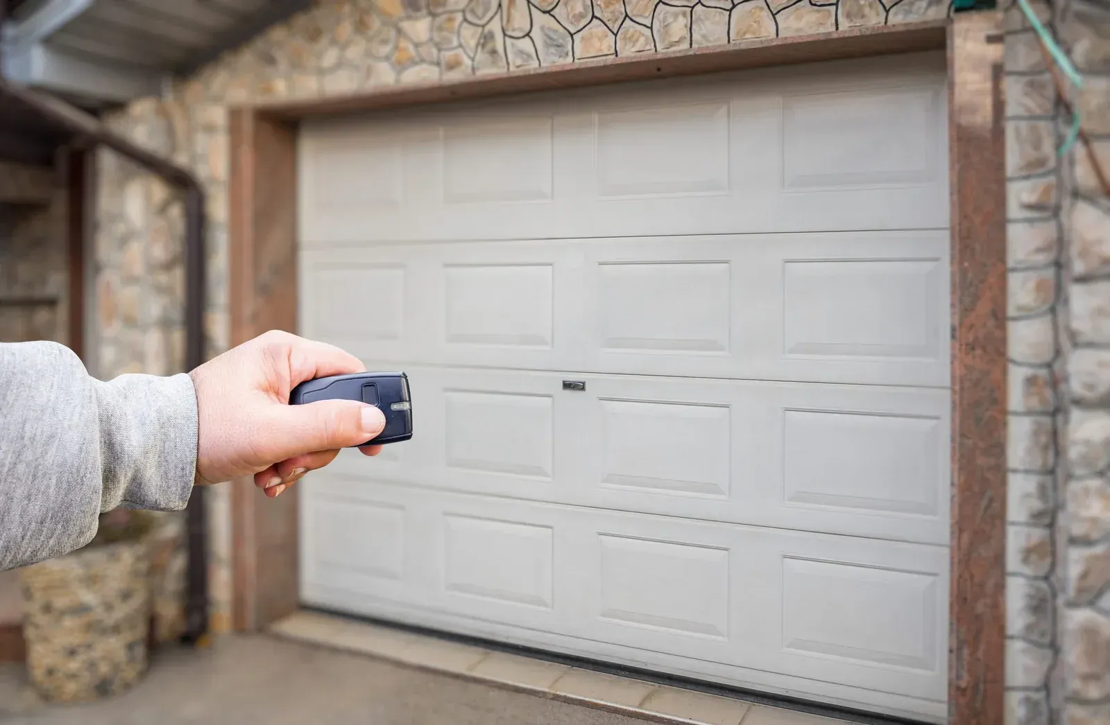 Hand holding a car key fob aimed at a closed white garage door