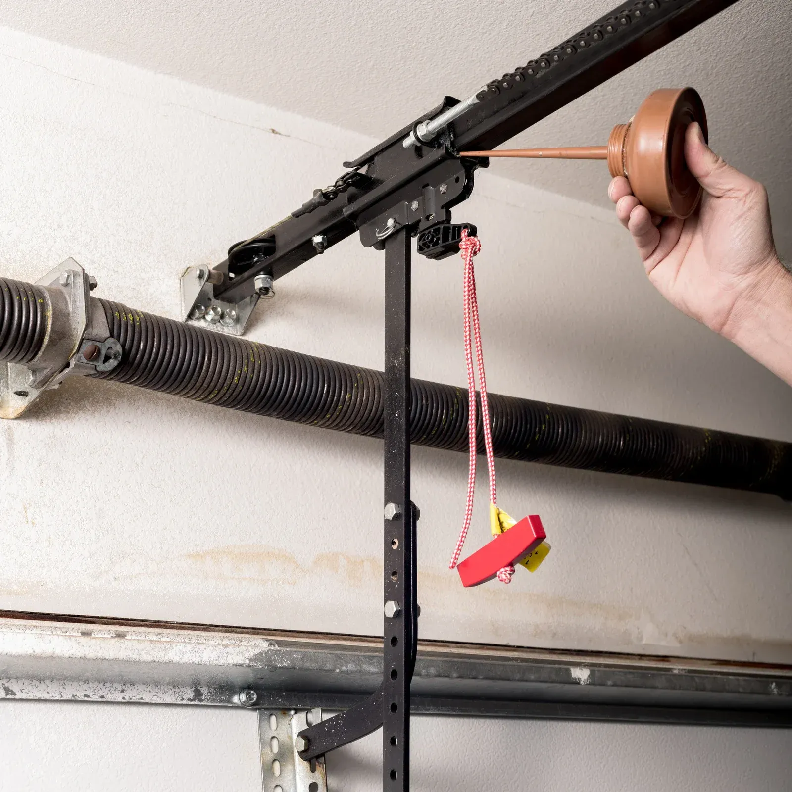 Garage door opener being manually pulled by a hand with a brown knob and red emergency release cord