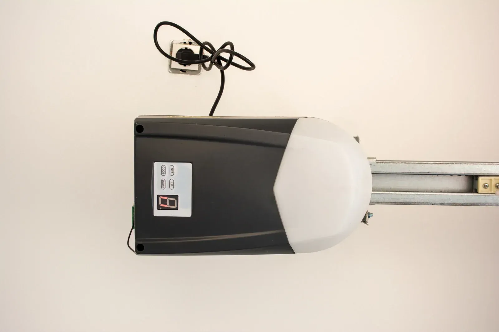 Black garage door opener mounted on a wall with a rail and hanging cord