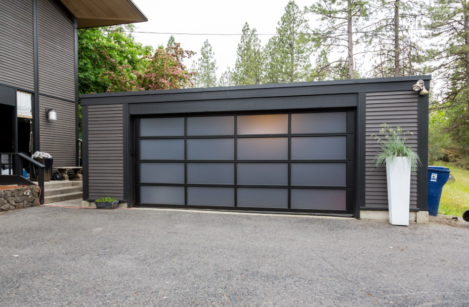 Modern black garage with frosted glass panels beside a house driveway