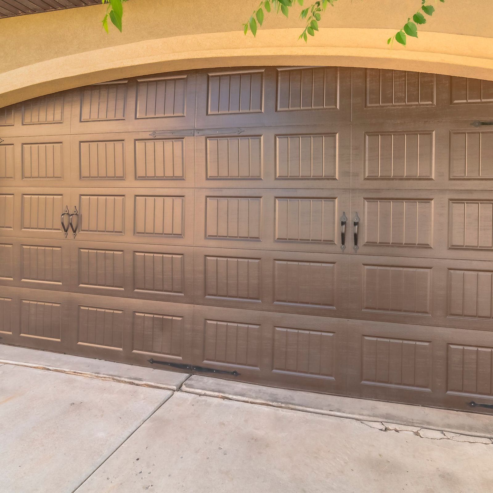 Brown double garage door with rectangular panels beneath a stucco archway