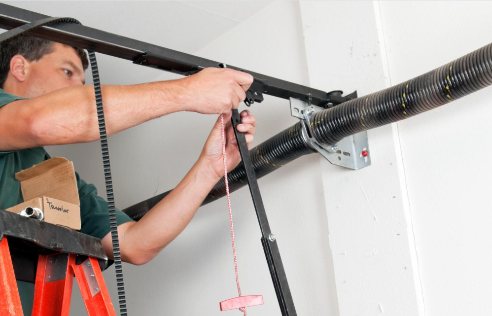 Technician installing a garage door opener motor overhead with tools and ladder nearby