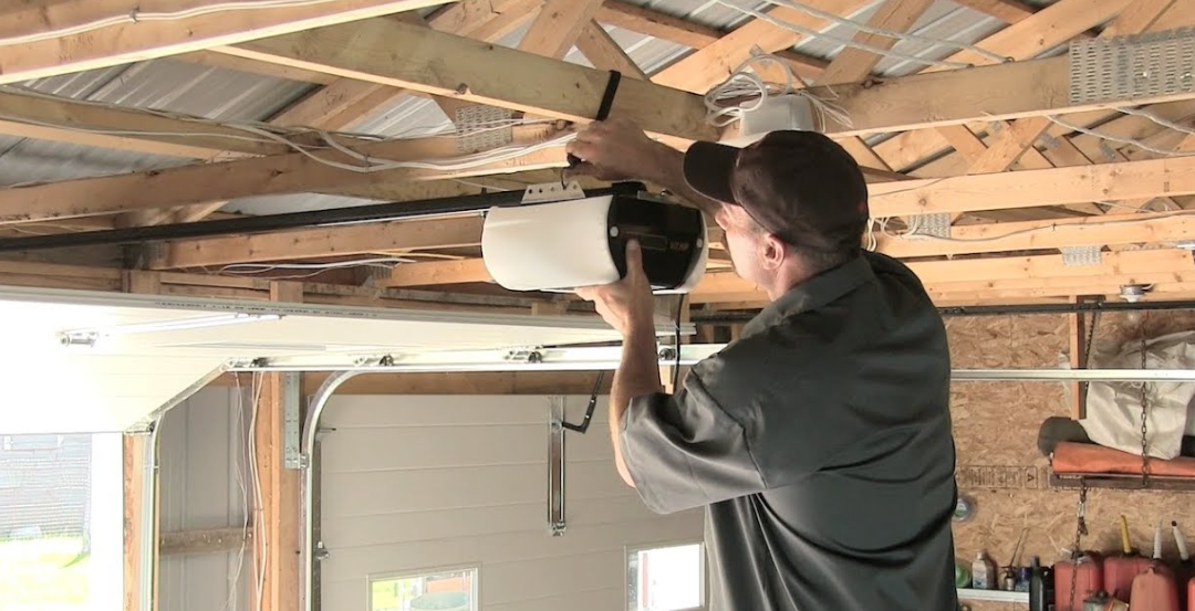 Person using a drill to install a ceiling fixture in an unfinished garage with exposed wooden rafters.