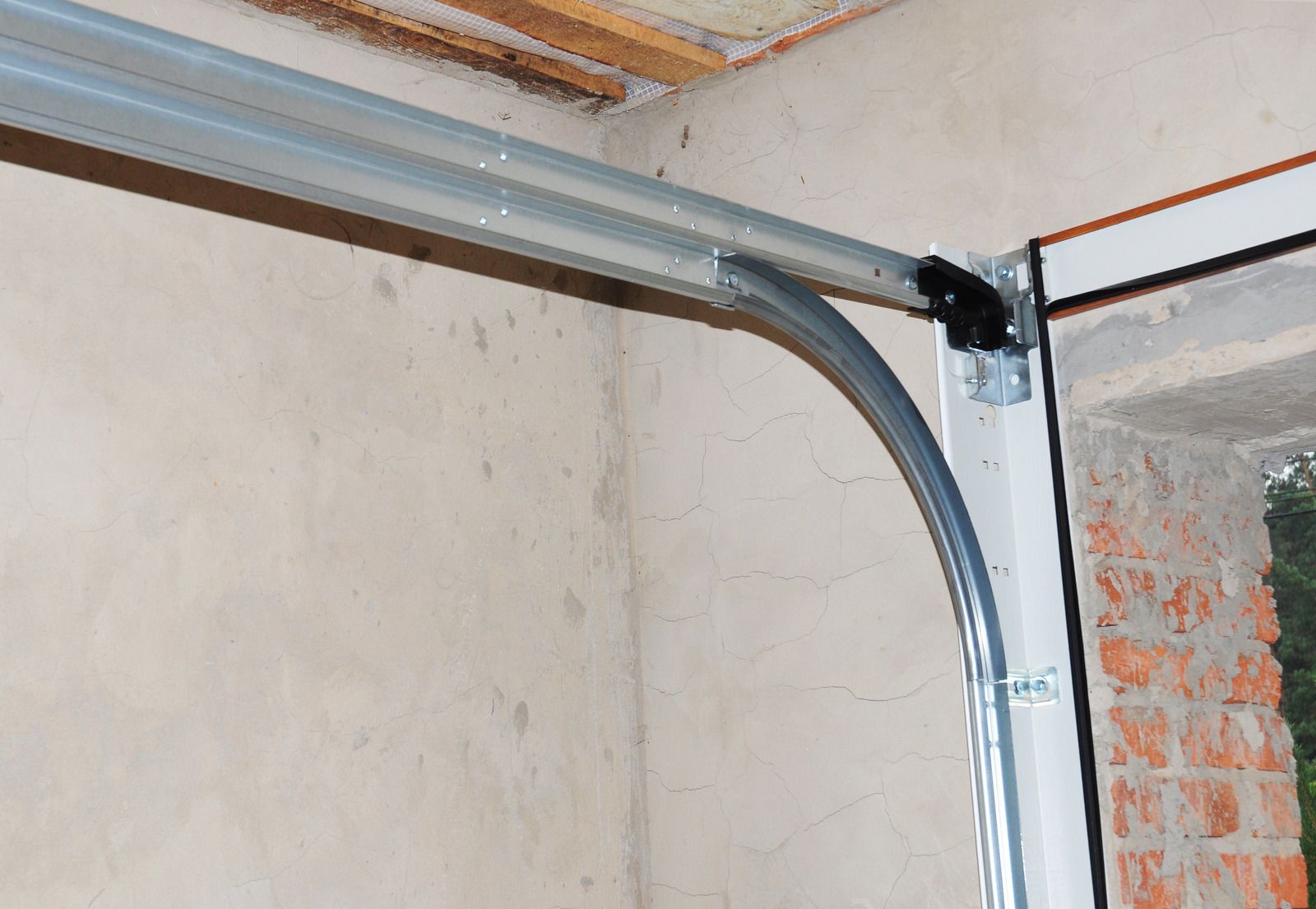 Curved metal garage door track mounted along a white wall near exposed brick and ceiling beams