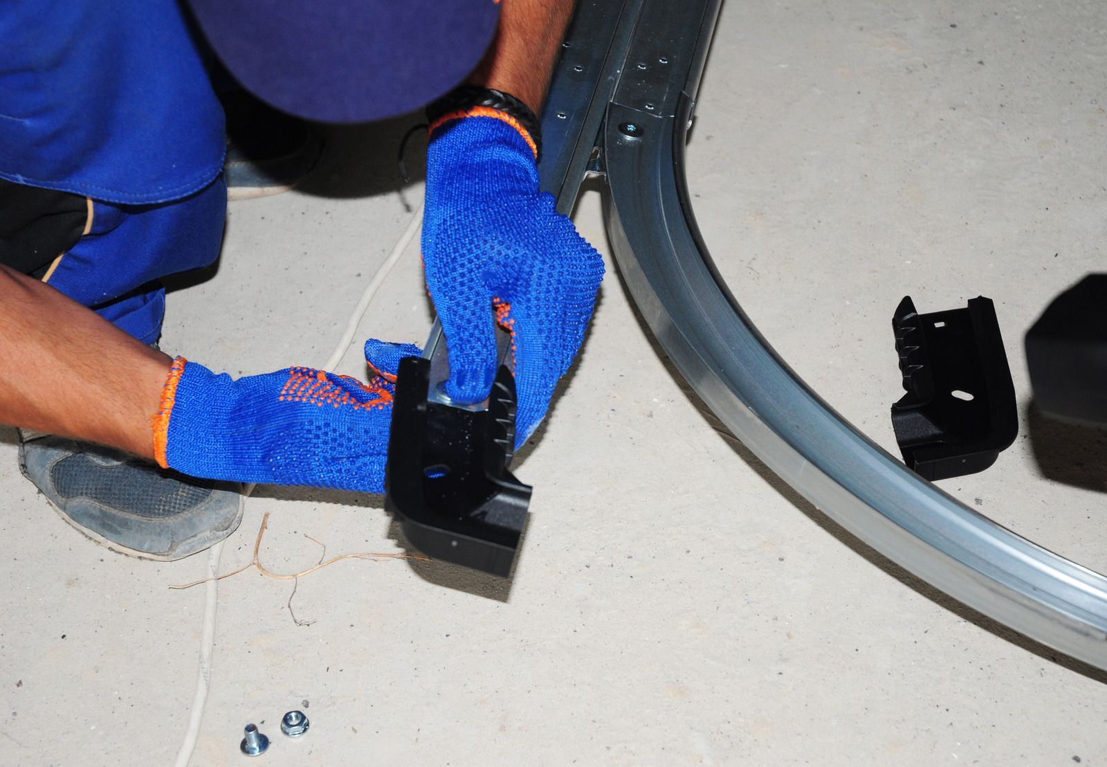 Gloved hands assembling a black plastic part beside a curved gray pipe on a floor