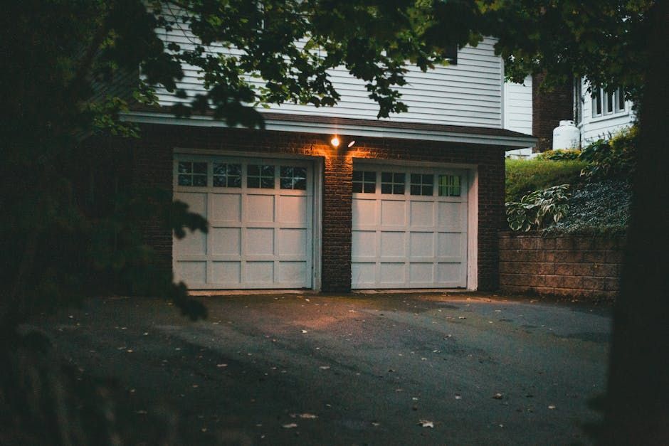 Driveway leading to a white two-car garage at dusk, framed by trees and brick walls