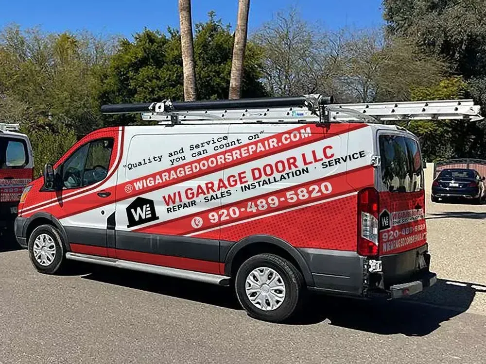 A white and red Wi Garage Door LLC service van parked outdoors with ladder racks on the roof.